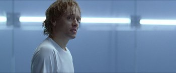 Movie still from “Headhunters” (2011), directed by Morten Tyldum – A man in a white t - shirt is standing in a room; Close Up shot, Low angle