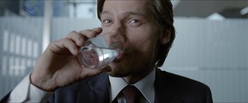 Movie still from “Headhunters” (2011), directed by Morten Tyldum – A person wearing a suit and tie drinking a glass of water; Close Up shot, Over the shoulder angle