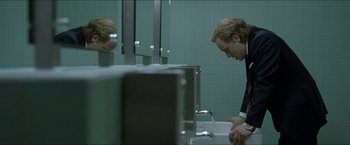 Movie still from “Headhunters” (2011), directed by Morten Tyldum – A man in a suit is washing his hands in a public bathroom; Medium shot, Low angle