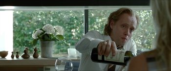 Movie still from “Headhunters” (2011), directed by Morten Tyldum – A man holding a bottle of wine in front of a window; Close Up shot, Low angle
