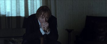 Movie still from “Headhunters” (2011), directed by Morten Tyldum – A man sitting in a chair with his hand to his face; Medium shot, Low angle
