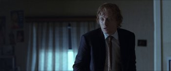 Movie still from “Headhunters” (2011), directed by Morten Tyldum – A man wearing a suit and tie standing in front of a window; Close Up shot, Over the shoulder angle