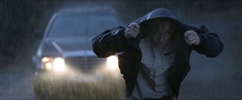 Movie still from “Headhunters” (2011), directed by Morten Tyldum – A woman in a jacket is holding her jacket over her head in the pouring rain; Medium shot, Low angle