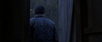 Movie still from “Headhunters” (2011), directed by Morten Tyldum – A man wearing a black jacket and a black hat looking out of a window; Wide shot, Over the shoulder angle