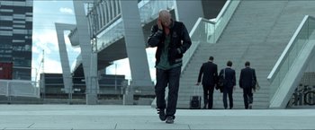 Movie still from “Headhunters” (2011), directed by Morten Tyldum – A man walking down the street talking on a cell phone; Wide shot, Low angle