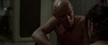 Movie still from “Headhunters” (2011), directed by Morten Tyldum – A man with a shaved head is looking at the camera; Close Up shot, Low angle