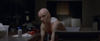 Movie still from “Headhunters” (2011), directed by Morten Tyldum – A man with a shaved head sitting at a table; Close Up shot, Over the shoulder angle