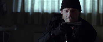 Movie still from “Headhunters” (2011), directed by Morten Tyldum – A man in black jacket and black hat holding a cell phone; Close Up shot, Low angle