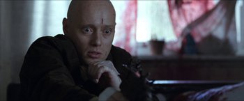Movie still from “Headhunters” (2011), directed by Morten Tyldum – A man with a shaved head is looking at the camera; Close Up shot, Low angle