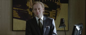 Movie still from “Headhunters” (2011), directed by Morten Tyldum – A man in a suit and tie standing in front of a painting; Close Up shot, Low angle