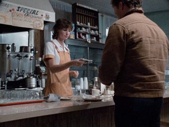 Movie still from “Henry: Portrait of a Serial Killer” (1986), directed by John McNaughton – A woman in an apron is standing at a counter; Medium shot, Over the shoulder angle