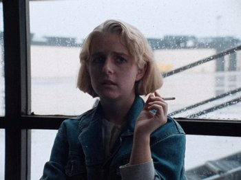 Movie still from “Henry: Portrait of a Serial Killer” (1986), directed by John McNaughton – A woman smoking a cigarette in front of an airplane window; Close Up shot, Low angle