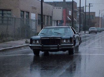 Movie still from “Henry: Portrait of a Serial Killer” (1986), directed by John McNaughton – A car is driving down the street on a rainy day; Wide shot, Low angle