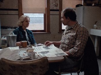 Movie still from “Henry: Portrait of a Serial Killer” (1986), directed by John McNaughton – A man and a woman sitting at a table with a newspaper; Medium shot, Over the shoulder angle