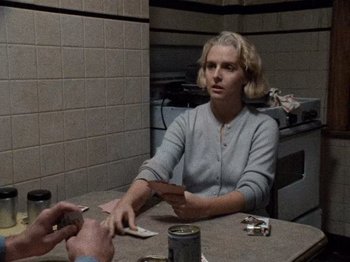 Movie still from “Henry: Portrait of a Serial Killer” (1986), directed by John McNaughton – A woman sitting at a table holding a card; Medium shot, Over the shoulder angle