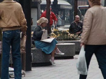 Movie still from “Henry: Portrait of a Serial Killer” (1986), directed by John McNaughton – A woman sitting on a bench on the sidewalk; Wide shot, High angle