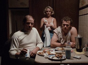 Movie still from “Henry: Portrait of a Serial Killer” (1986), directed by John McNaughton – A group of people sitting at a table with plates of food on it; Medium shot, High angle