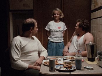 Movie still from “Henry: Portrait of a Serial Killer” (1986), directed by John McNaughton – A group of people sitting at a table with plates of food; Medium shot, Over the shoulder angle
