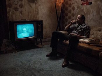 Movie still from “Henry: Portrait of a Serial Killer” (1986), directed by John McNaughton – A man sitting in front of an old television; Wide shot, High angle