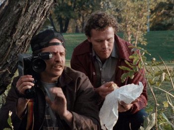 Movie still from “Henry: Portrait of a Serial Killer” (1986), directed by John McNaughton – A man holding a camera while another man looks at a piece of paper; Medium shot, High angle