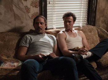 Movie still from “Henry: Portrait of a Serial Killer” (1986), directed by John McNaughton – A couple of men sitting on top of a brown couch; Medium shot, Low angle
