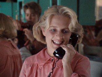 Movie still from “Henry: Portrait of a Serial Killer” (1986), directed by John McNaughton – A woman talking on a phone in front of other people; Close Up shot, Over the shoulder angle