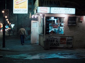 Movie still from “Henry: Portrait of a Serial Killer” (1986), directed by John McNaughton – A man walking down the street in front of a store; Wide shot, High angle