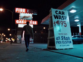 Movie still from “Henry: Portrait of a Serial Killer” (1986), directed by John McNaughton – A man walking down the street in front of a gas station; Wide shot, Low angle