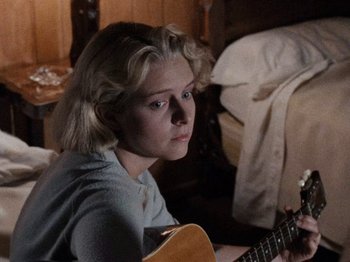 Movie still from “Henry: Portrait of a Serial Killer” (1986), directed by John McNaughton – A woman sitting in front of an acoustic guitar; Close Up shot, Low angle