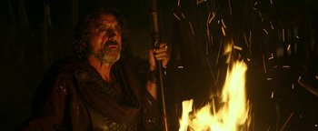 Movie still from “Hercules” (2014), directed by Brett Ratner – An old man holding a stick in front of a fire; Medium shot, Low angle