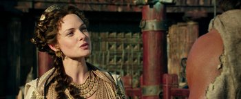 Movie still from “Hercules” (2014), directed by Brett Ratner – A woman wearing a gold necklace standing in front of a building; Close Up shot, Over the shoulder angle
