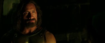Movie still from “Hercules” (2014), directed by Brett Ratner – A man with long hair and a beard is standing in the dark; Close Up shot, Over the shoulder angle