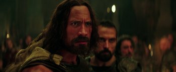 Movie still from “Hercules” (2014), directed by Brett Ratner – A man with long hair and a goatee is looking at the camera; Close Up shot, Over the shoulder angle