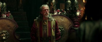 Movie still from “Hercules” (2014), directed by Brett Ratner – An old man with a long beard wearing a red and gold outfit; Medium shot, Over the shoulder angle
