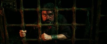 Movie still from “Hercules” (2014), directed by Brett Ratner – A man with a beard is looking through the bars of a jail cell; Medium shot, Low angle