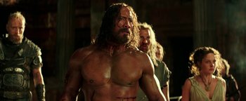 Movie still from “Hercules” (2014), directed by Brett Ratner – A man with long hair is standing in front of two other men; Medium shot, Over the shoulder angle