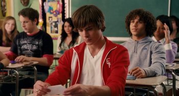 Movie still from “High School Musical 3: Senior Year” (2008), directed by Kenny Ortega – A man sitting at a desk in front of other people; Medium shot, Over the shoulder angle