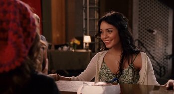 Movie still from “High School Musical 3: Senior Year” (2008), directed by Kenny Ortega – A woman sitting at a dinner table smiling at the camera; Medium shot, Over the shoulder angle