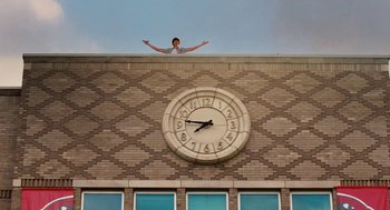 Movie still from “High School Musical 3: Senior Year” (2008), directed by Kenny Ortega – A man standing on the side of a building with his arms outstretched; Extreme Wide shot, Low angle