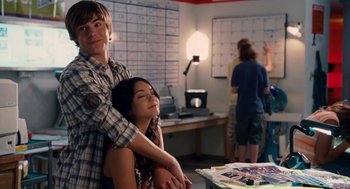 Movie still from “High School Musical 3: Senior Year” (2008), directed by Kenny Ortega – A man and a woman hugging in front of a desk; Medium shot, Over the shoulder angle