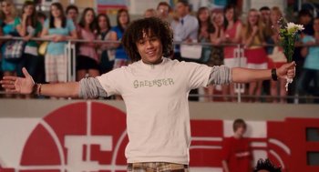 Movie still from “High School Musical 3: Senior Year” (2008), directed by Kenny Ortega – A young man is smiling while standing in front of an audience; Medium shot, Low angle
