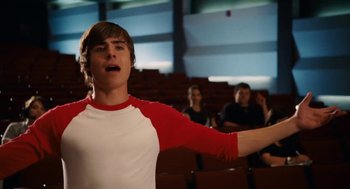Movie still from “High School Musical 3: Senior Year” (2008), directed by Kenny Ortega – A man in a red and white shirt is singing; Medium shot, Low angle