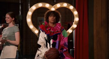 Movie still from “High School Musical 3: Senior Year” (2008), directed by Kenny Ortega – A man dressed as a clown holding a basketball in front of a heart; Wide shot, Low angle