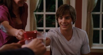 Movie still from “High School Musical 3: Senior Year” (2008), directed by Kenny Ortega – A man sitting at a table with a cup in front of him; Medium shot, Over the shoulder angle
