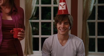 Movie still from “High School Musical 3: Senior Year” (2008), directed by Kenny Ortega – A young man wearing a paper party hat while sitting in front of a window; Medium shot, Over the shoulder angle
