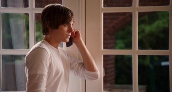 Movie still from “High School Musical 3: Senior Year” (2008), directed by Kenny Ortega – A man talking on a cell phone in front of a window; Medium shot, Over the shoulder angle