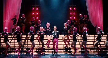 Movie still from “High School Musical 3: Senior Year” (2008), directed by Kenny Ortega – A group of people performing on a stage with a man standing in front of them; Wide shot, Low angle