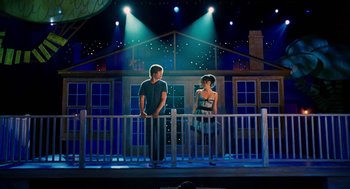 Movie still from “High School Musical 3: Senior Year” (2008), directed by Kenny Ortega – Two people standing on a stage in front of a building; Wide shot, Low angle