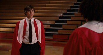 Movie still from “High School Musical 3: Senior Year” (2008), directed by Kenny Ortega – A young man in a graduation gown standing in front of stairs; Medium shot, Over the shoulder angle