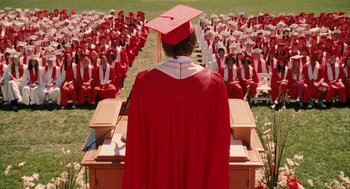 Movie still from “High School Musical 3: Senior Year” (2008), directed by Kenny Ortega – A group of people sitting in the grass with one person wearing a red graduation cap; Wide shot, High angle
